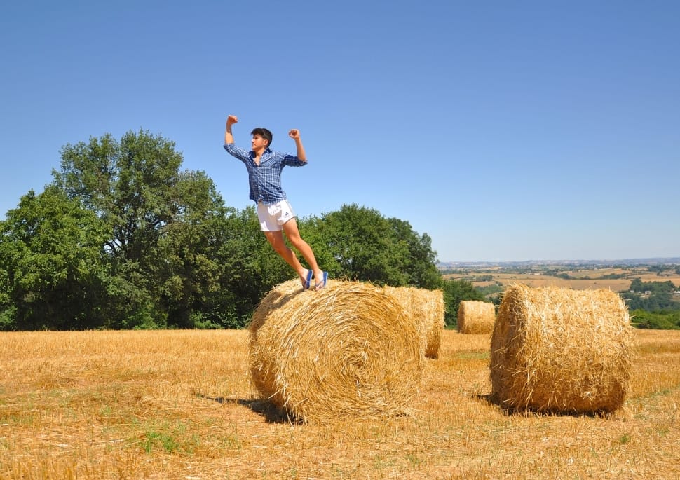 person in blue dress shirt and white pant jumping on brown hay during daytime preview