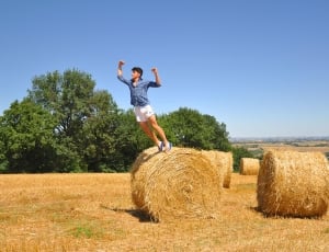 person in blue dress shirt and white pant jumping on brown hay during daytime thumbnail