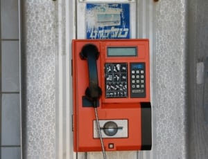 red and black coin operated telephone on wall during daytime thumbnail