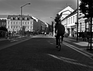 man riding on bicycle on gray pavement near concrete buildings thumbnail