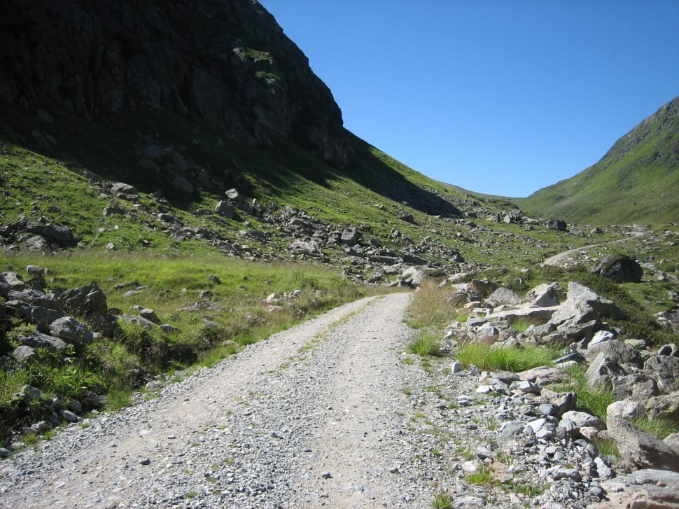white stony alley way in between green bush field on feet of mountain during daytime preview