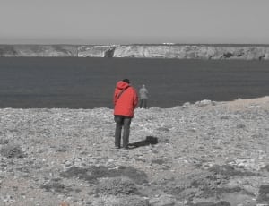 man in red jacket standing near the lake thumbnail