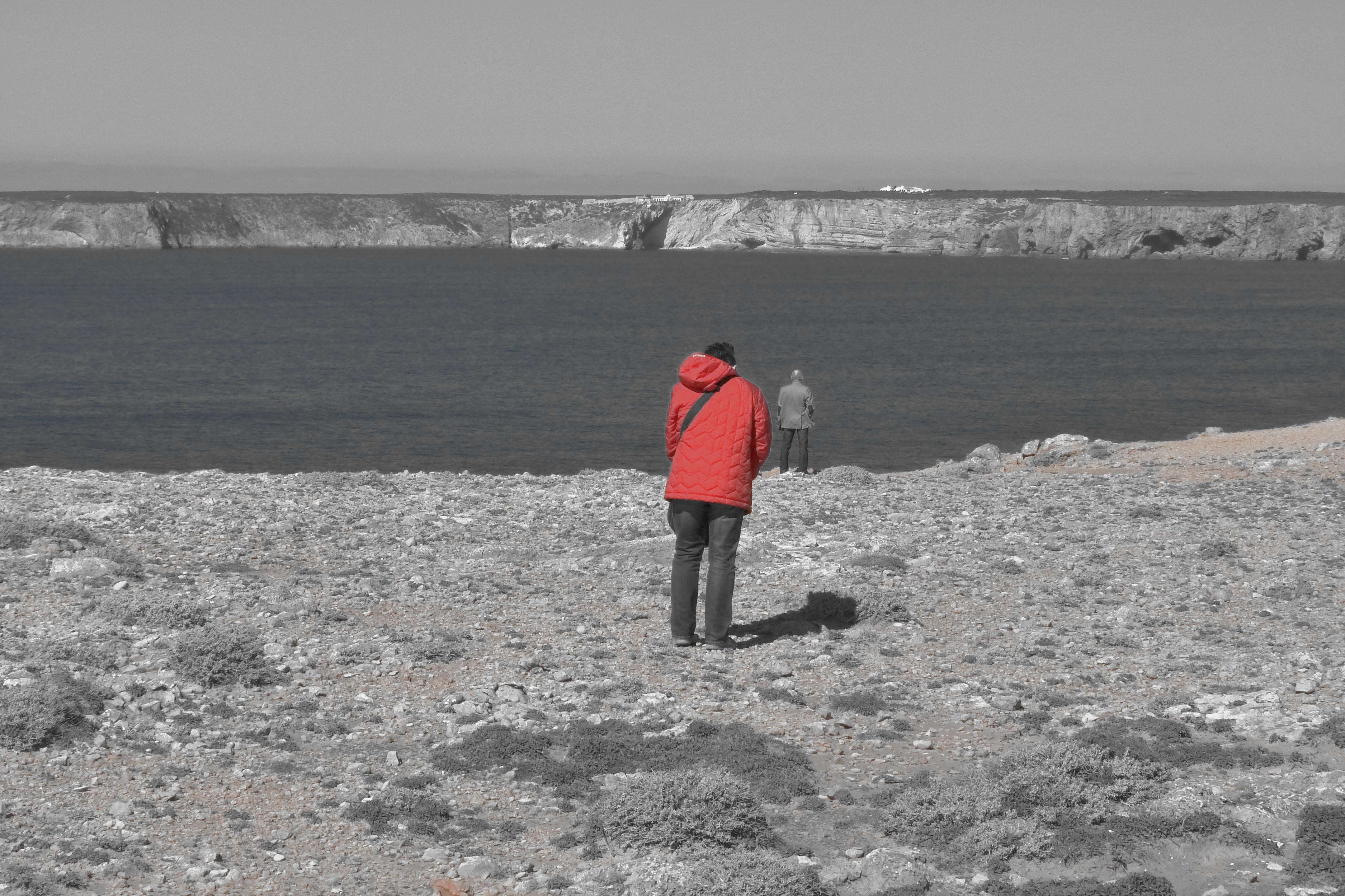 man in red jacket standing near the lake
