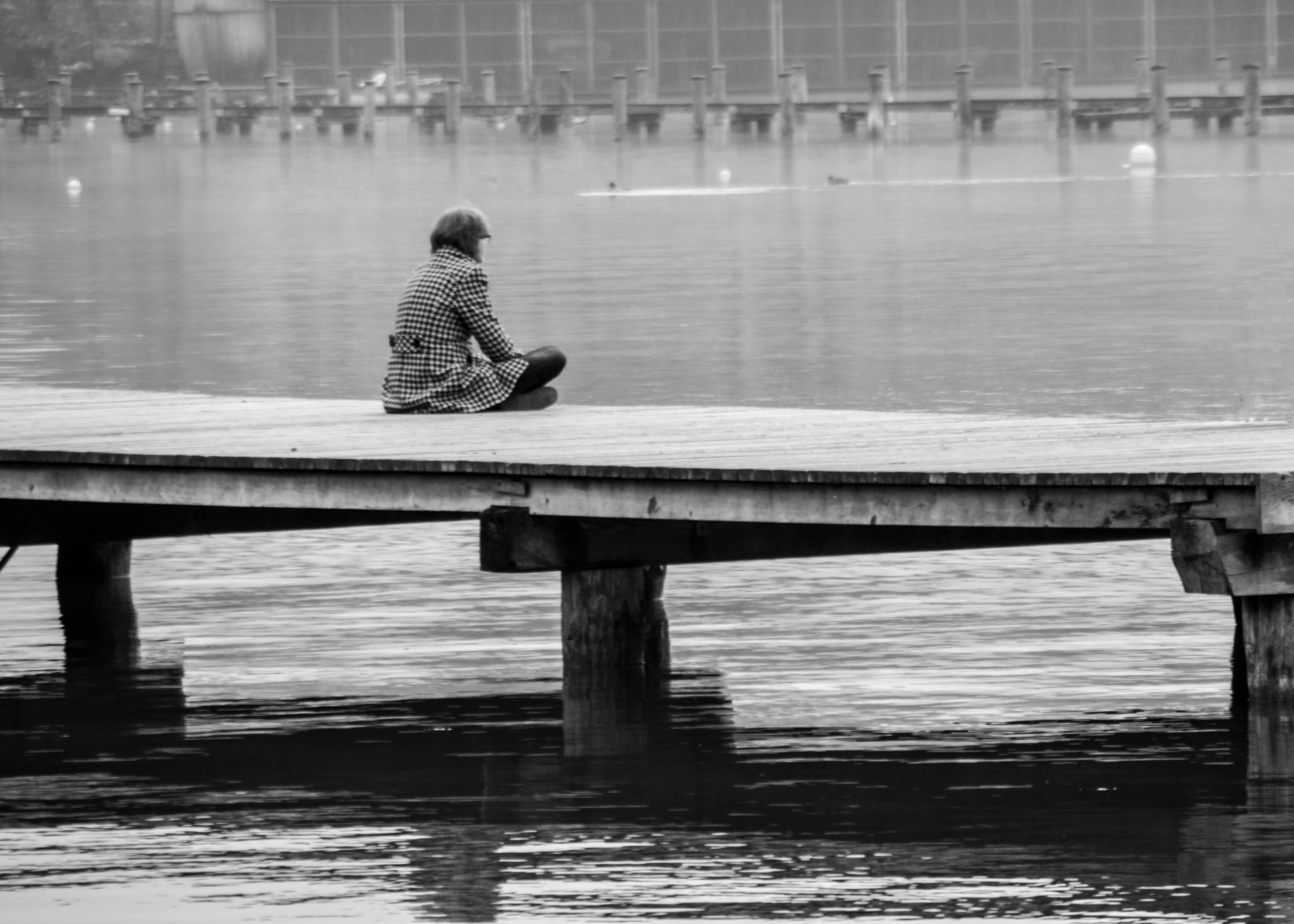 grayscale photography of woman sitting on wooden dock