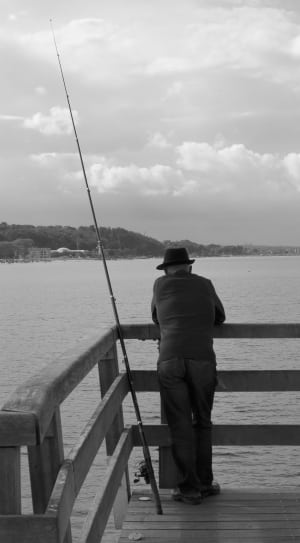 man in dock near on fishing rod grayscale photograph thumbnail