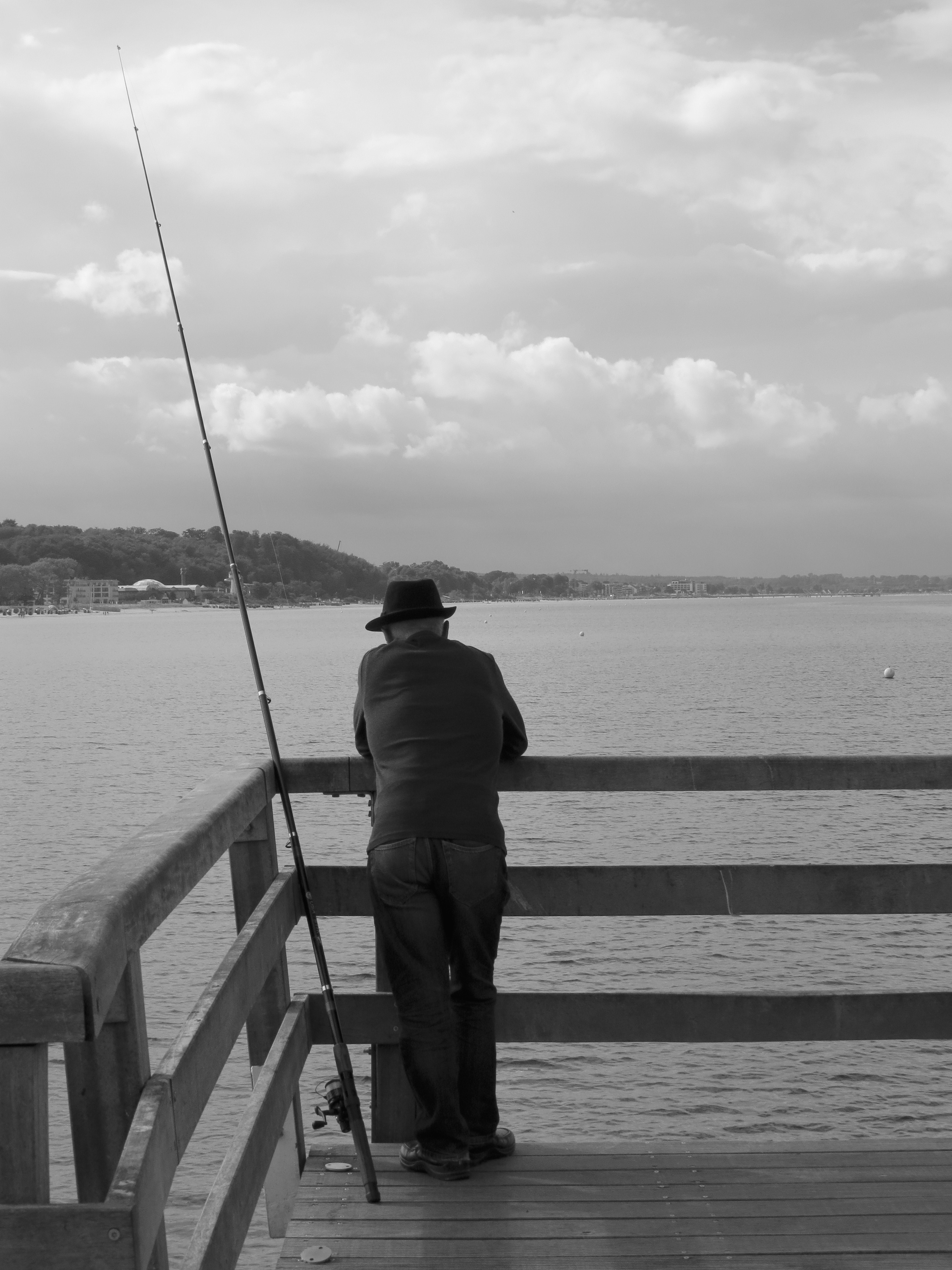 man in dock near on fishing rod grayscale photograph