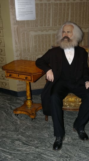 bearded man in black suit sitting on wooden armchair thumbnail