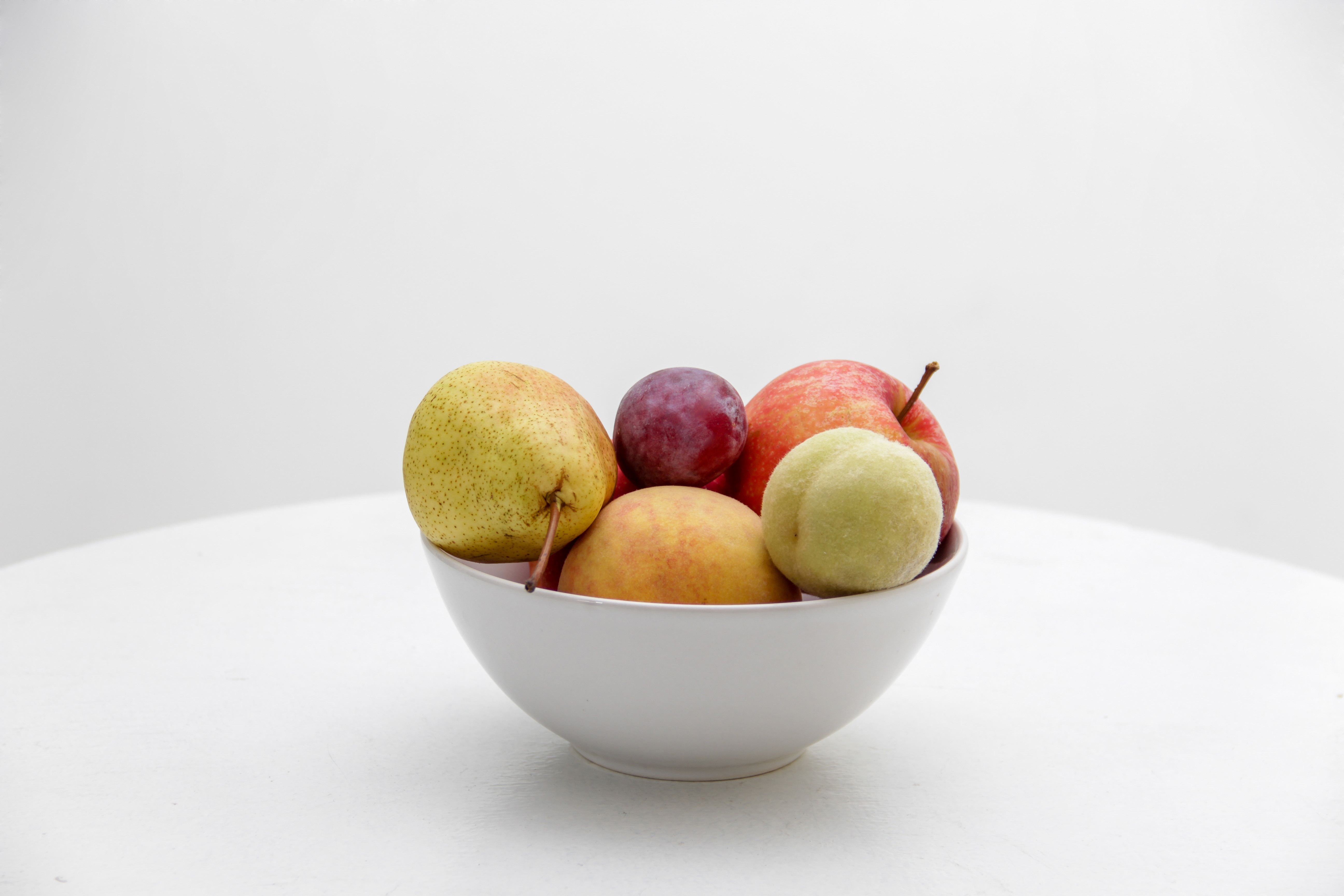 red and green apple with red grape and pear fruit on white ceramic bowl