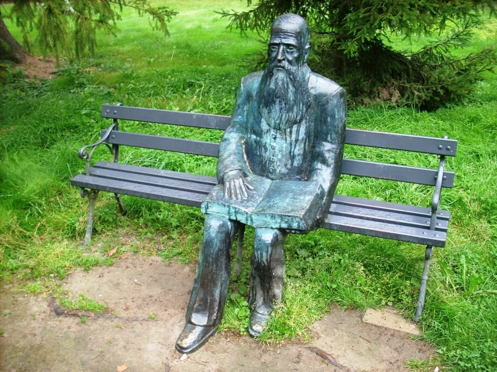 man sitting on bench with open book grey and green statue preview