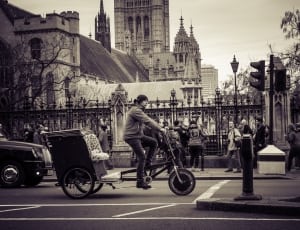 grayscale photography of man riding bicycle trike near building with gate at road thumbnail