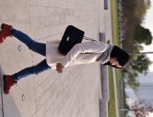 woman in white sweater and blue denim pants walking in daytime thumbnail