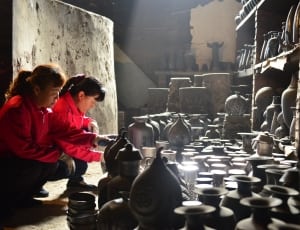 two woman wearing red jackets molding clay pots thumbnail
