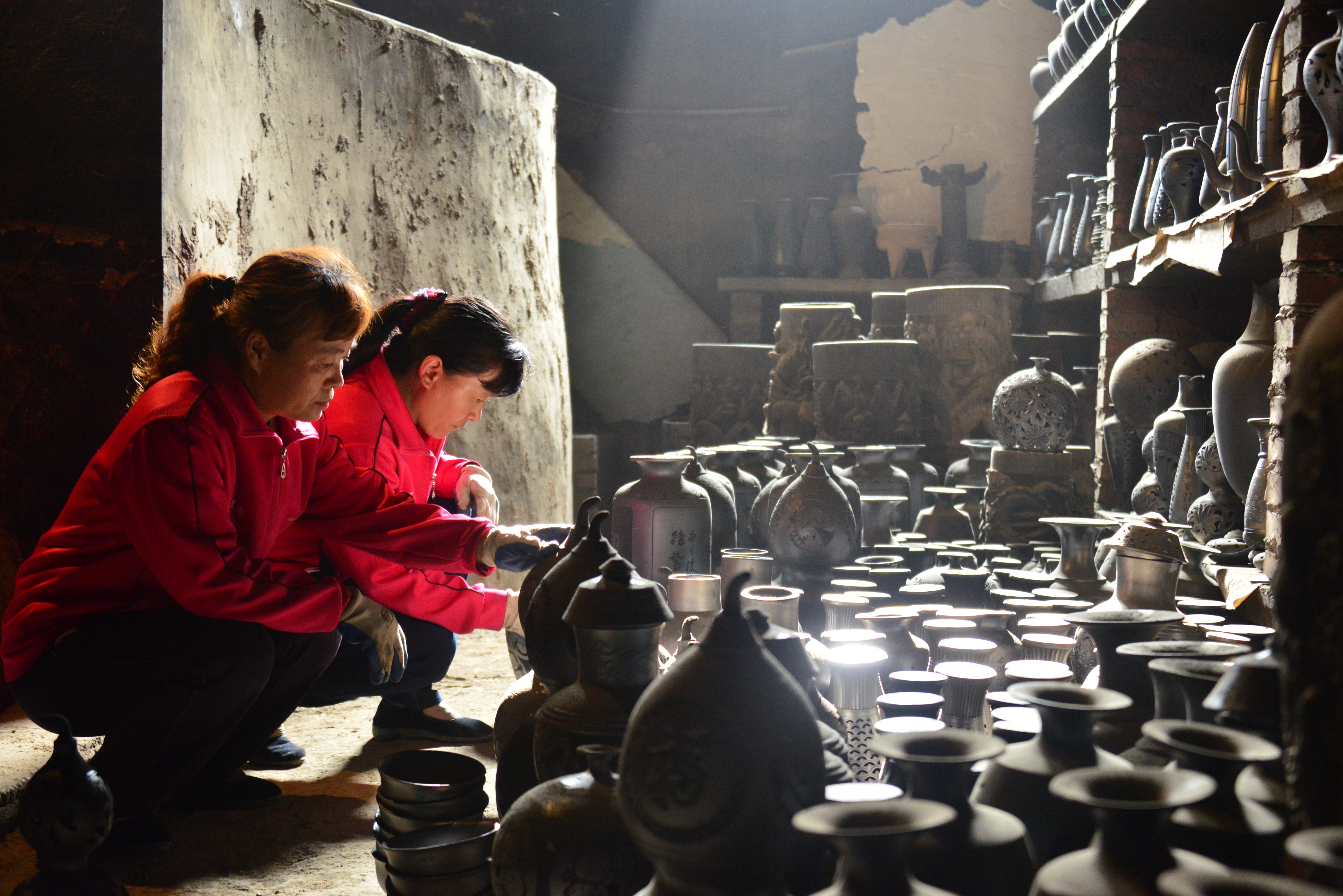two woman wearing red jackets molding clay pots