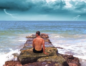 male in black shorts sitting on rock near beach thumbnail