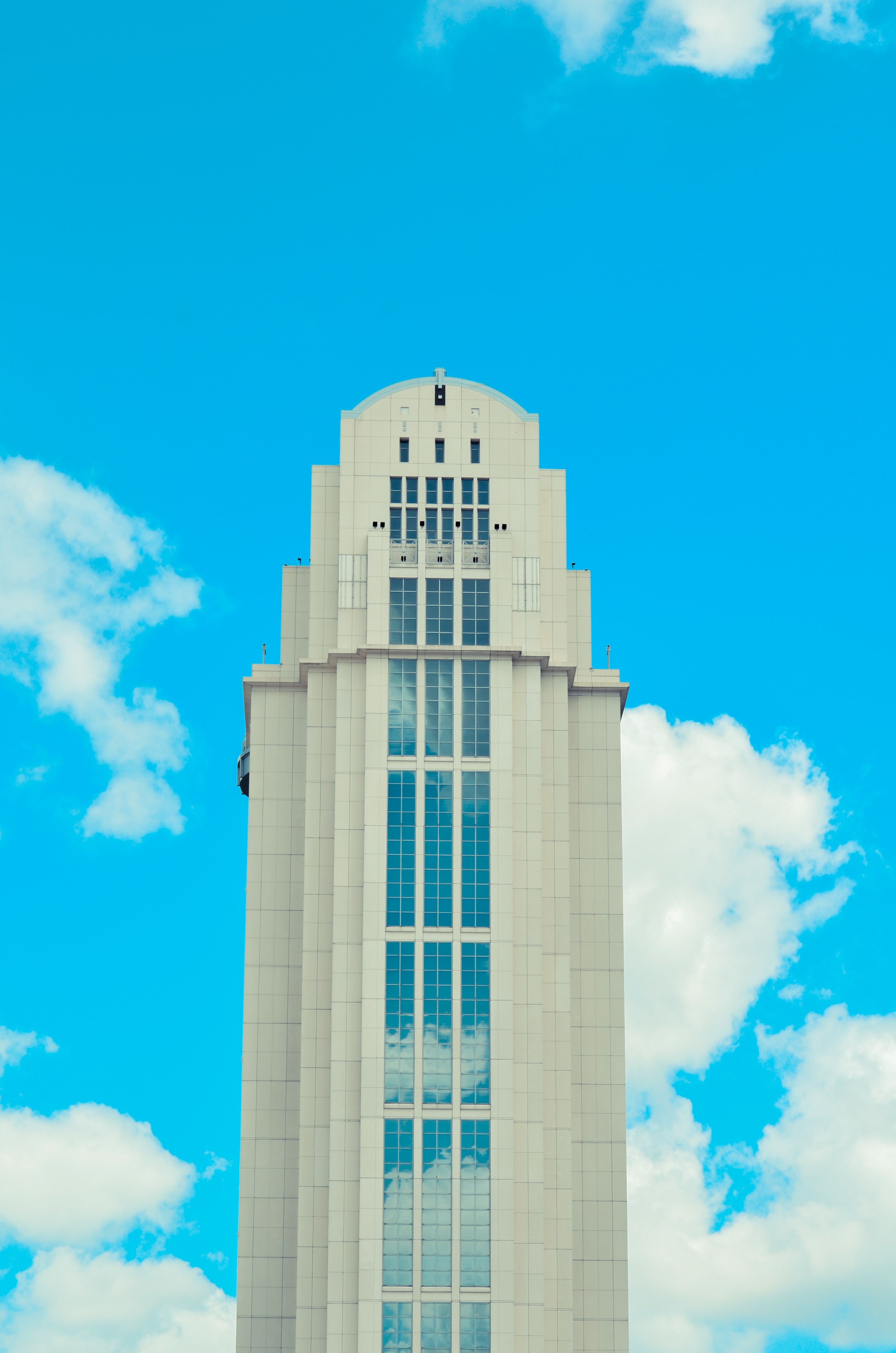 low angle view photo of white high-rise building under blue sky with cumulus clouds