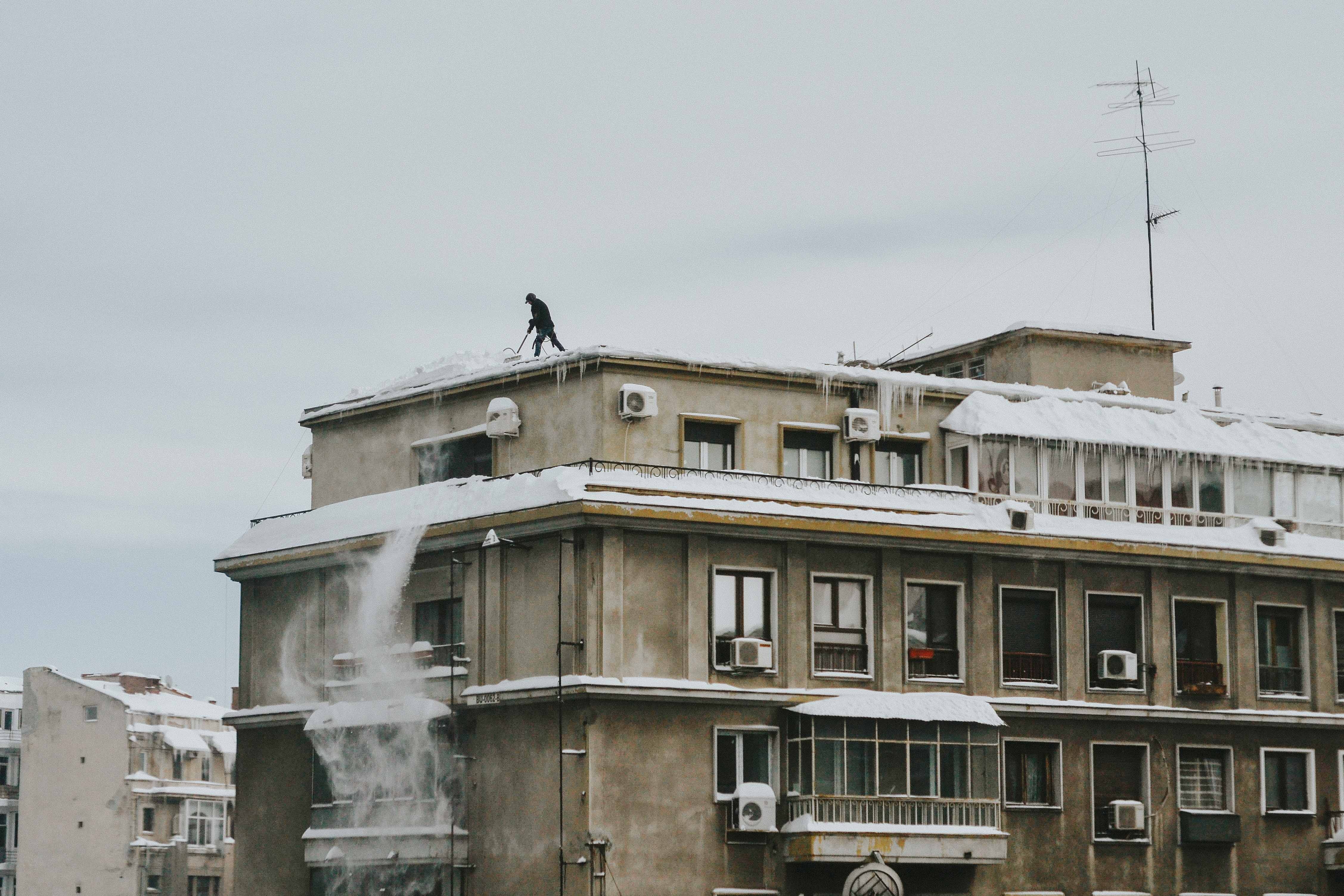 man on top of building removing the snow