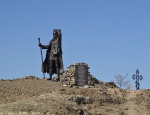 moses statue on brown dirt and cross statue at distance during daytime thumbnail