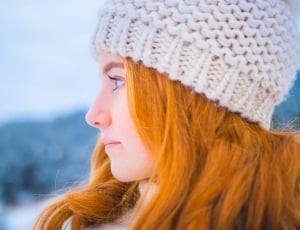 close photo of woman with orange hair wearing white knit cap thumbnail