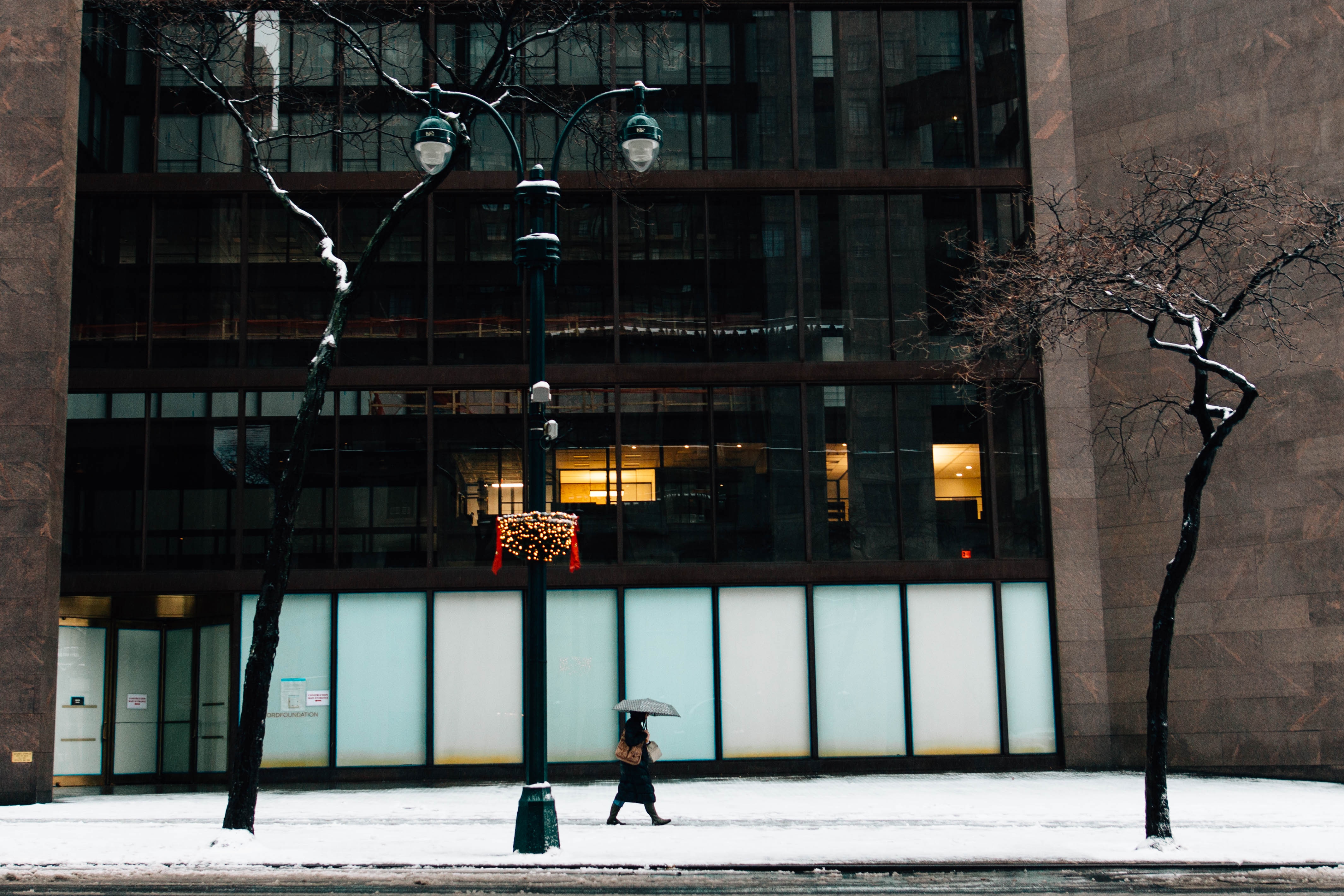 person walking on snow covered sidewalk near brown building during daytime