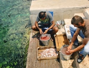 two man cleaning fish in using knife and metal bucket thumbnail