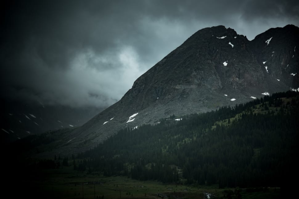 mountain near beside forest under black clouds during daytime preview