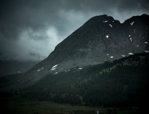 mountain near beside forest under black clouds during daytime thumbnail