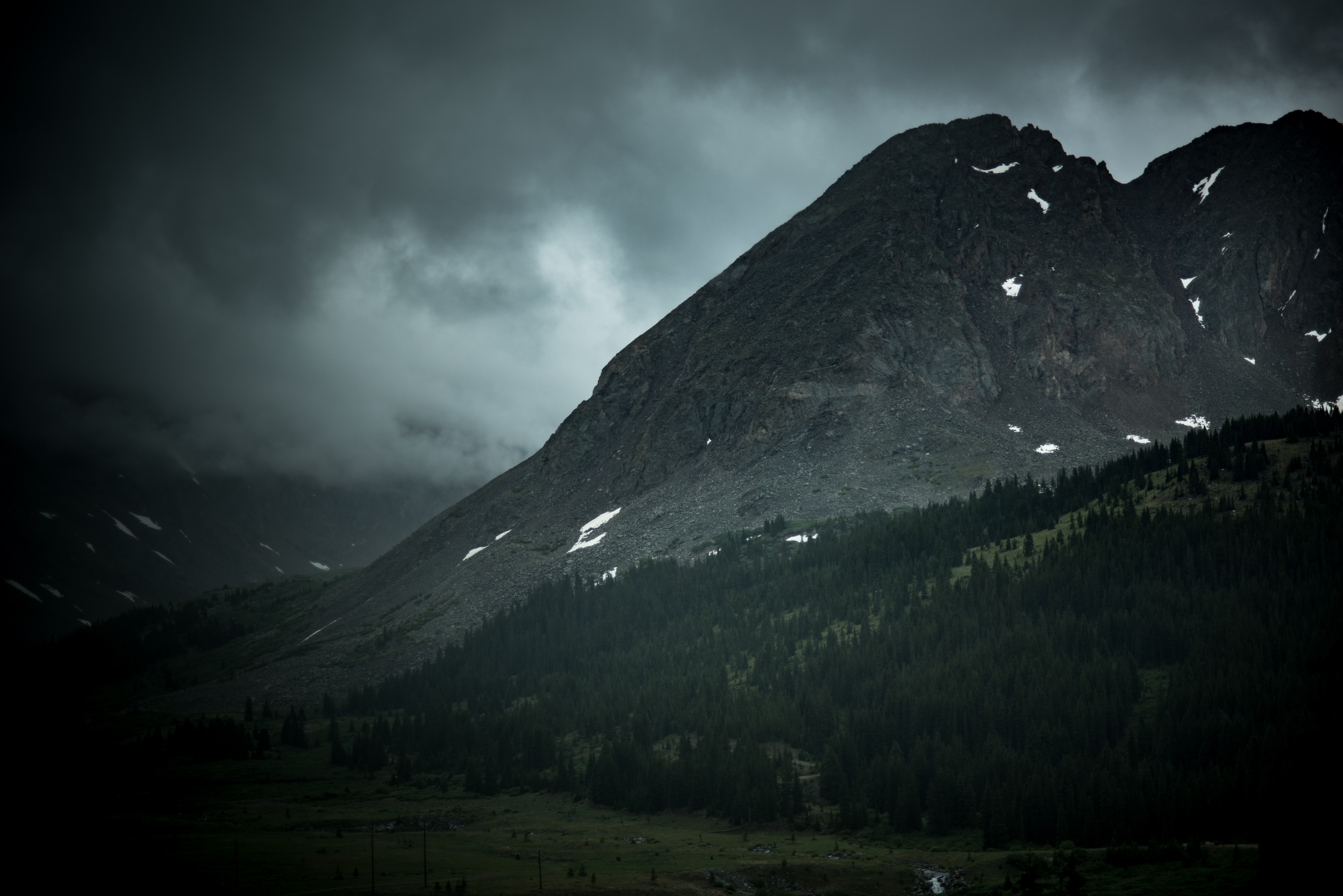 mountain near beside forest under black clouds during daytime