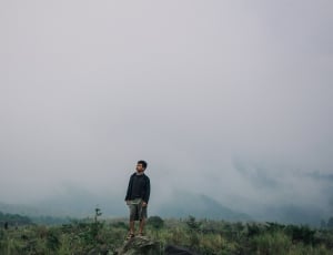 man in black sweater shirt standing on rock formation surrounded by green grasses thumbnail