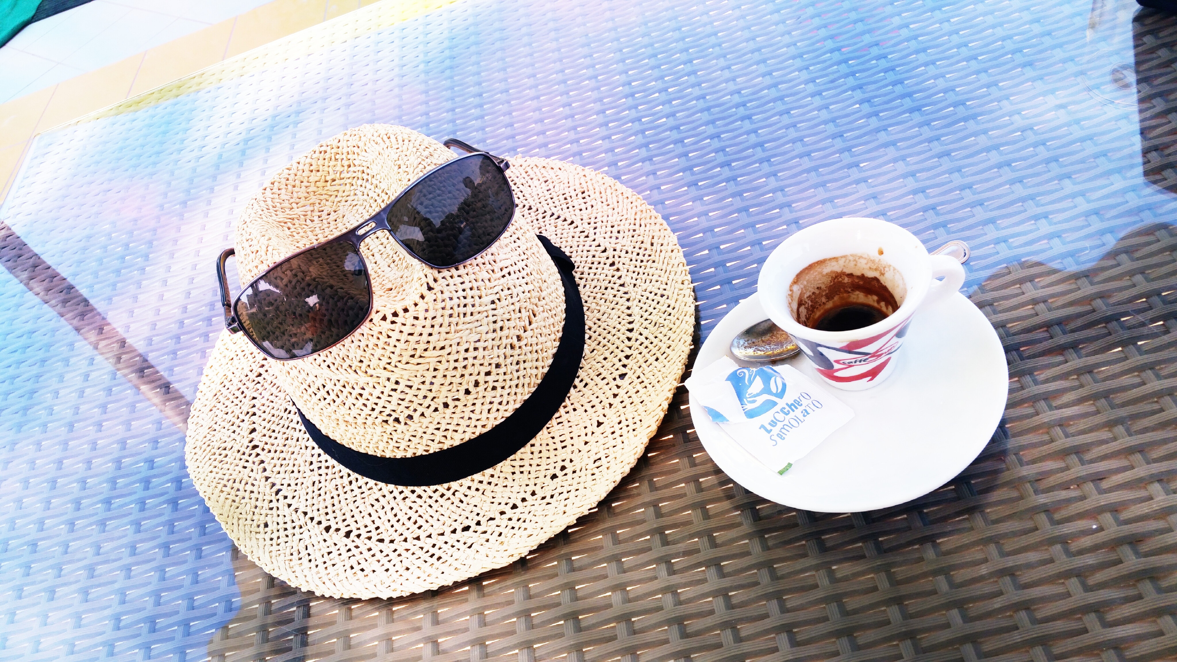 ceramic mug and saucer filled with coffee and brown hat and dark lens sunglasses