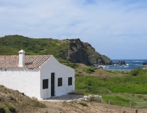 white concrete house near hill and beach photo thumbnail