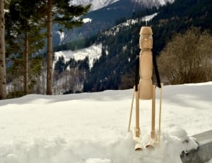 brown and black wooden puppet standing on snow surrounded with trees at daytime thumbnail