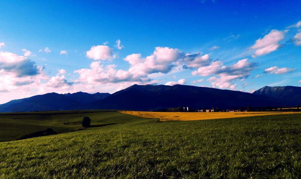 green grass field near mountain under white cloud blue skies preview