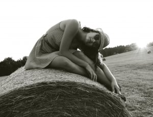 greyscale photo of woman wearing dress sitting on roll hay thumbnail