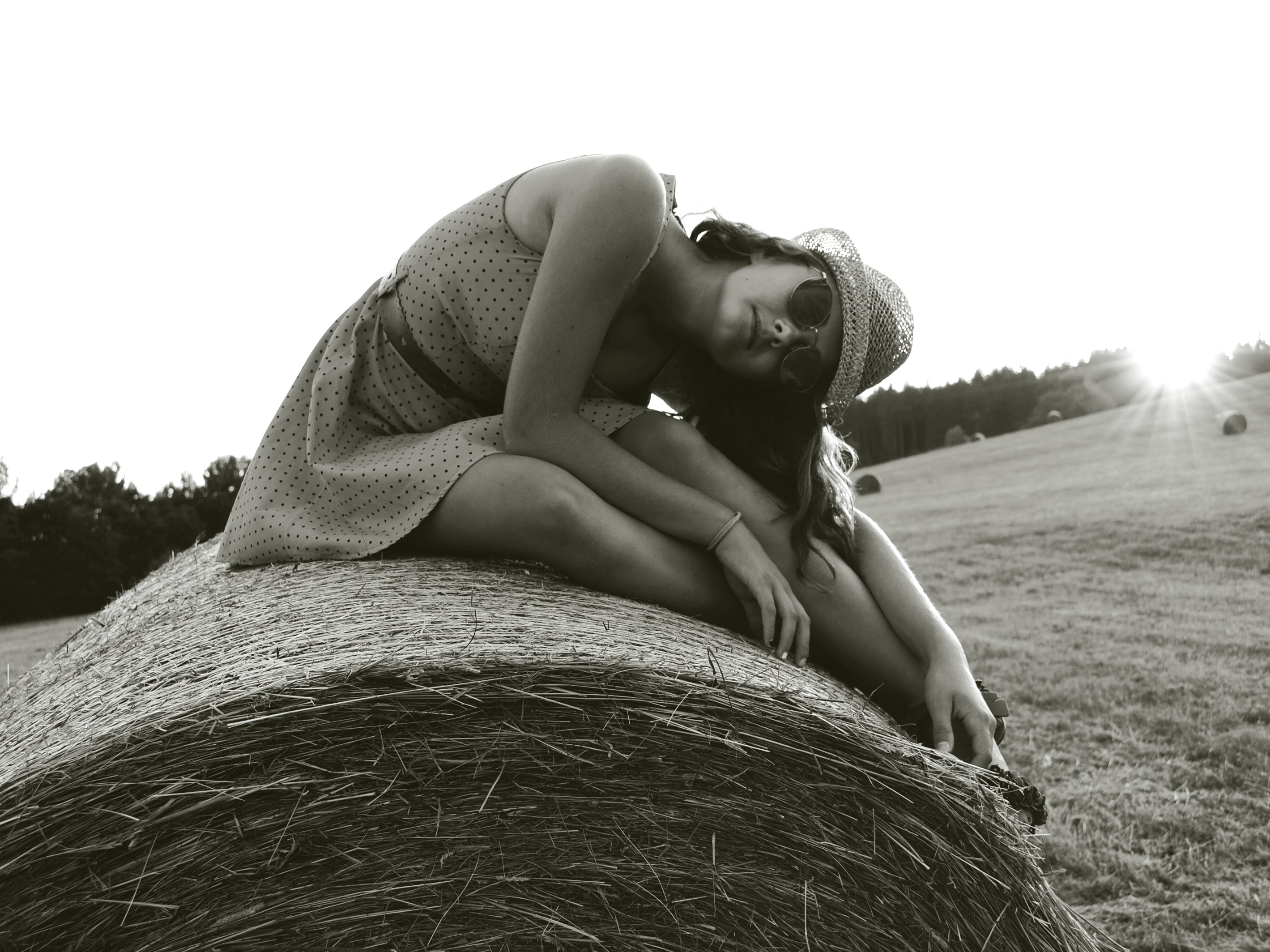 greyscale photo of woman wearing dress sitting on roll hay