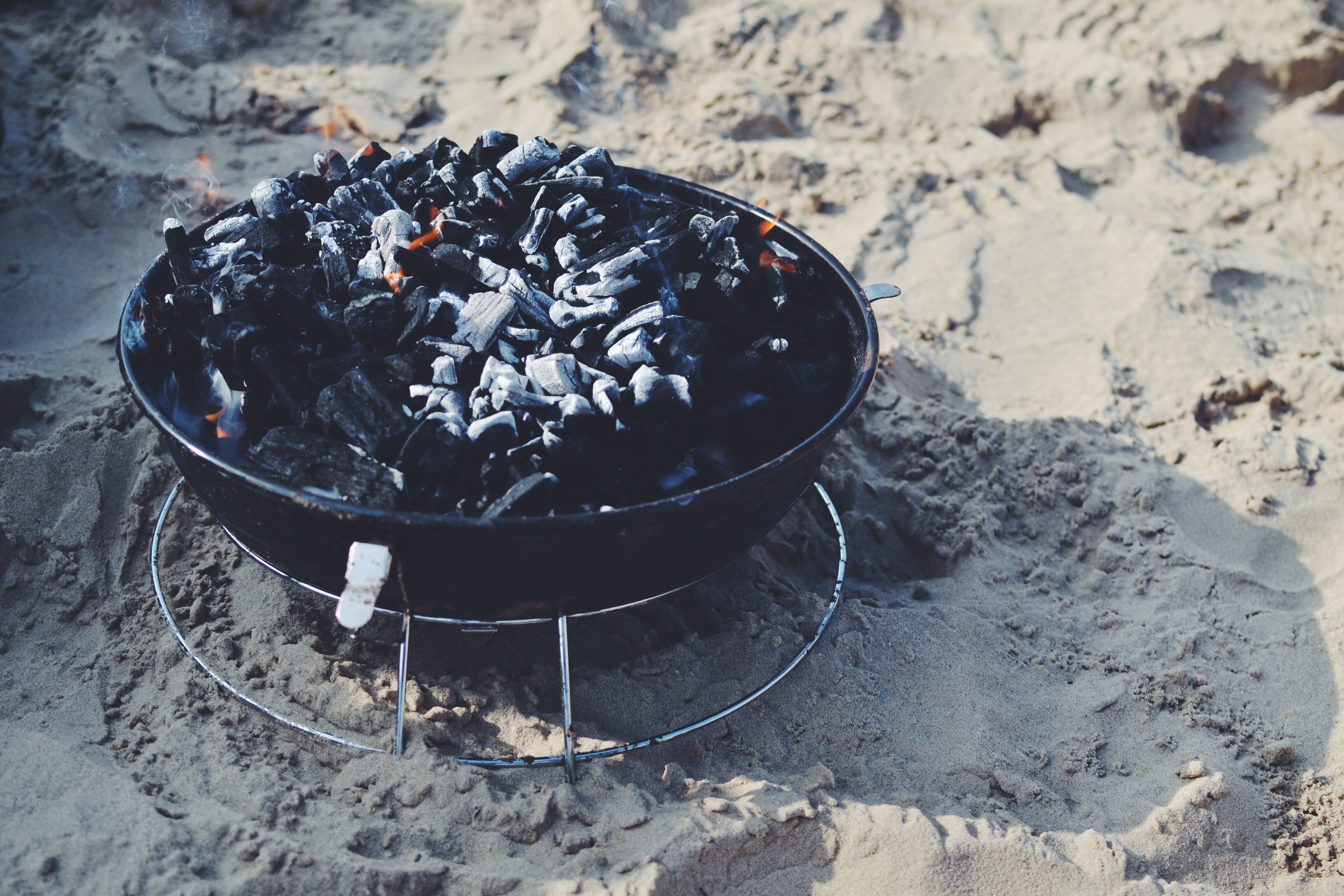 black charcoal grill with charcoal on sand