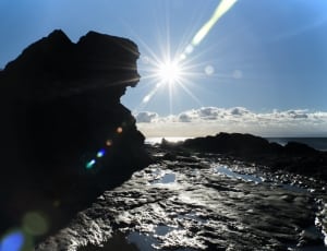 silhouette of rock formation near body of water under blue sky thumbnail