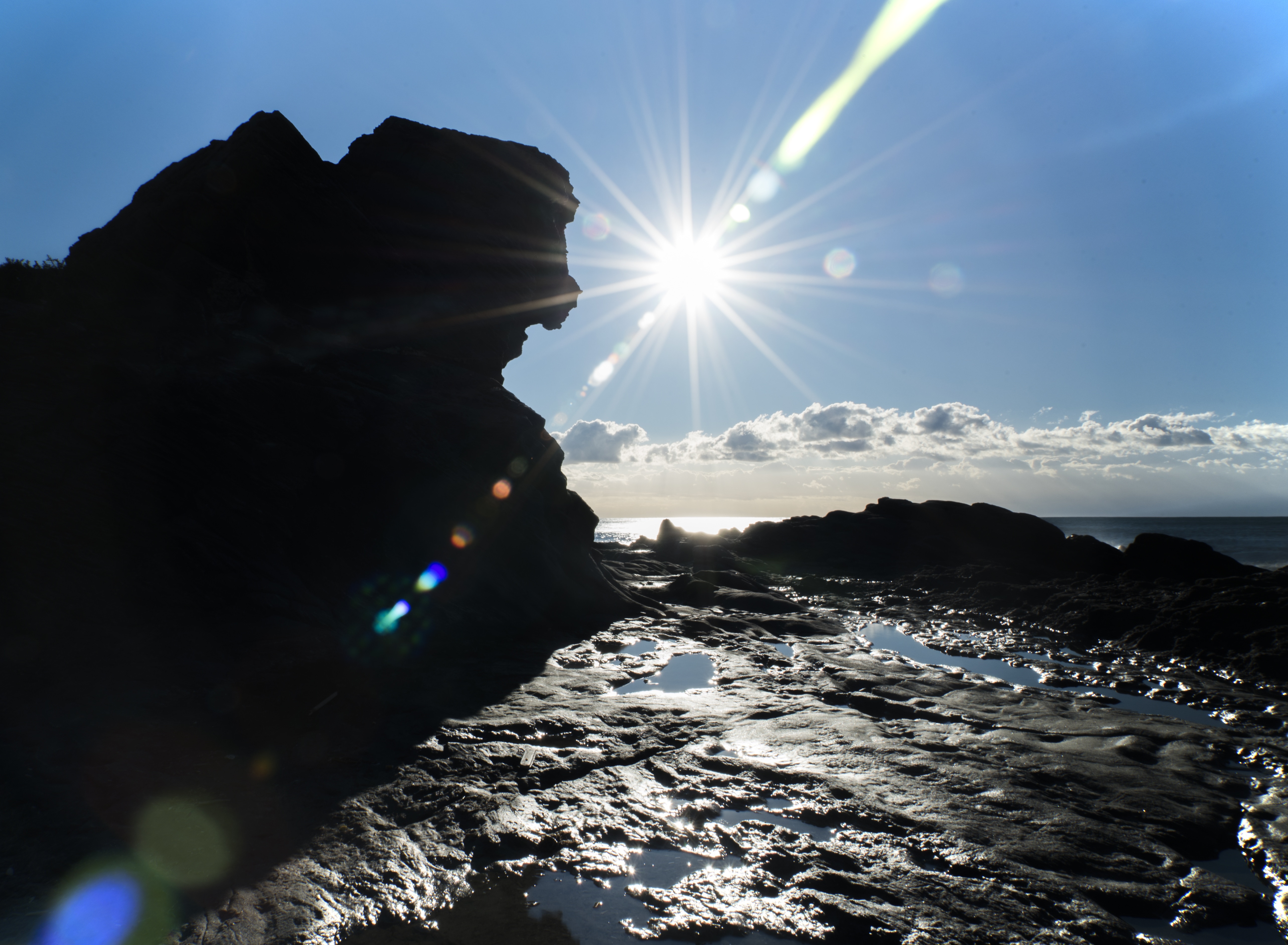 silhouette of rock formation near body of water under blue sky