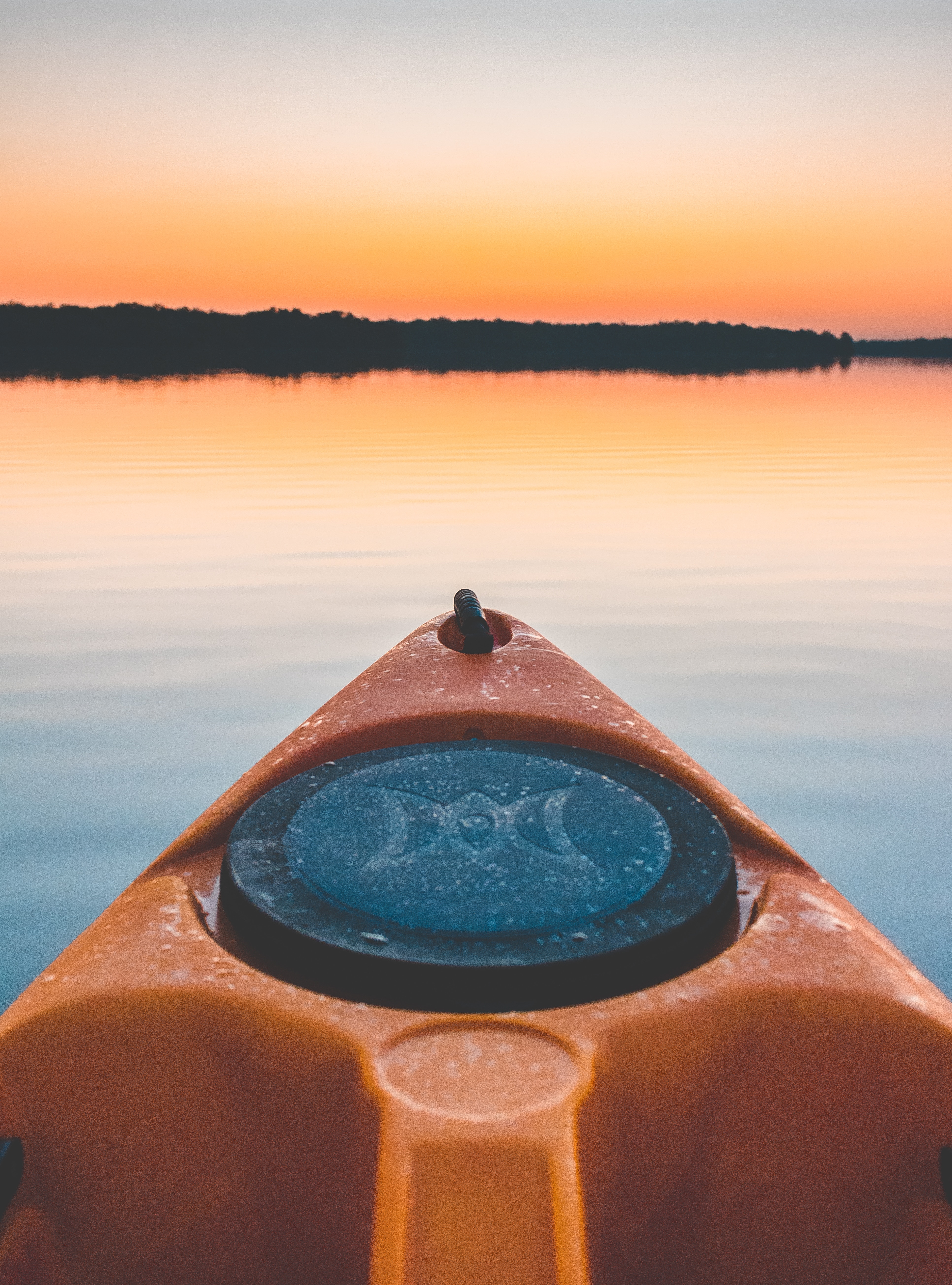 close up photo of a black and yellow kayak in lake near island during sunset