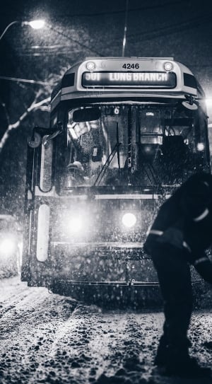 grayscale photo of person in front of tram shoveling snow during nighttime thumbnail