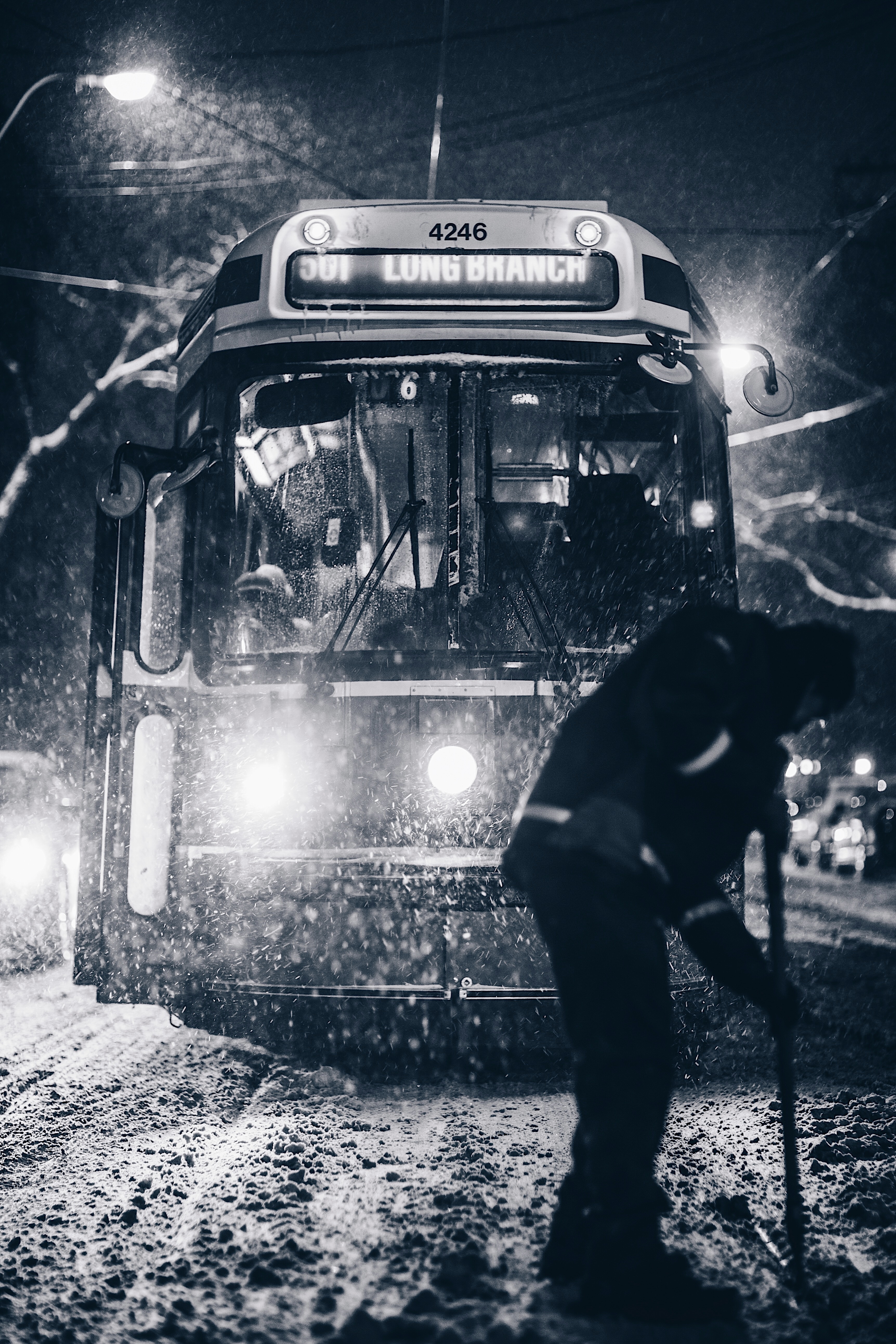 grayscale photo of person in front of tram shoveling snow during nighttime