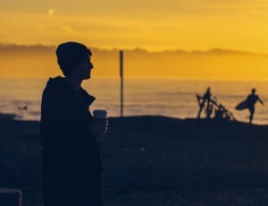 silhouette photography of a man holding his cup near ocean shoreline during golden hour thumbnail