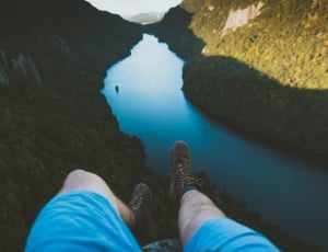 man in blue shorts sitting on rock near river at daytime thumbnail