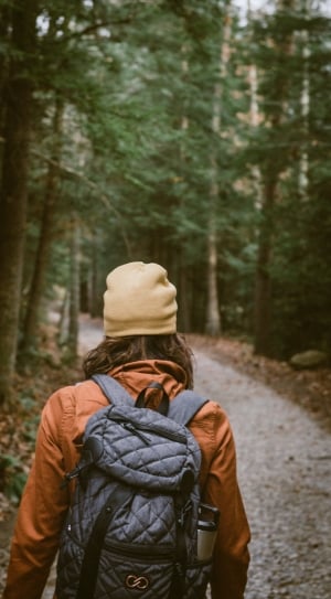 woman wearing brown jacket carrying a backpack walking at the forest thumbnail