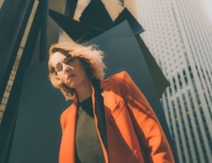 low angle photography of woman wearing orange coat, black undershirt near black and beige building thumbnail