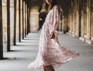 woman in pink long-sleeved tea-length dress standing in between concrete columns during daytime thumbnail