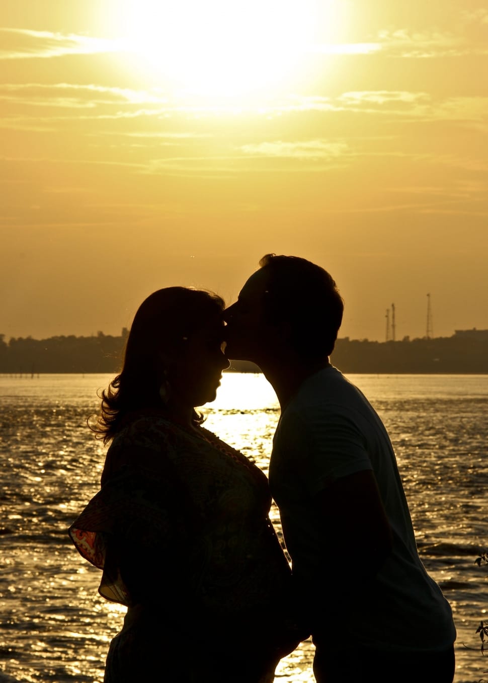 silhouette of man kissing woman near body of water during sunset preview