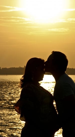 silhouette of man kissing woman near body of water during sunset thumbnail