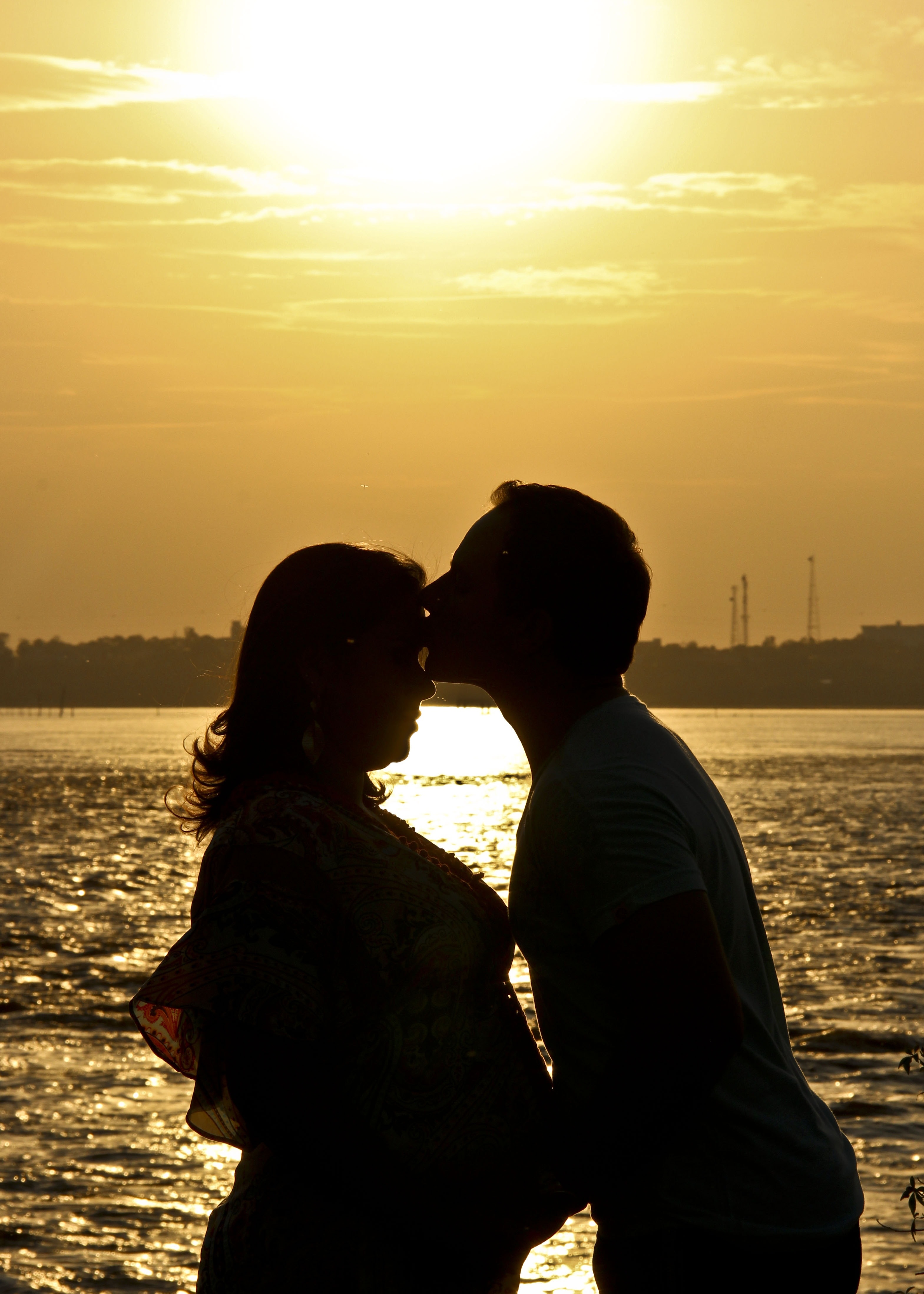 silhouette of man kissing woman near body of water during sunset
