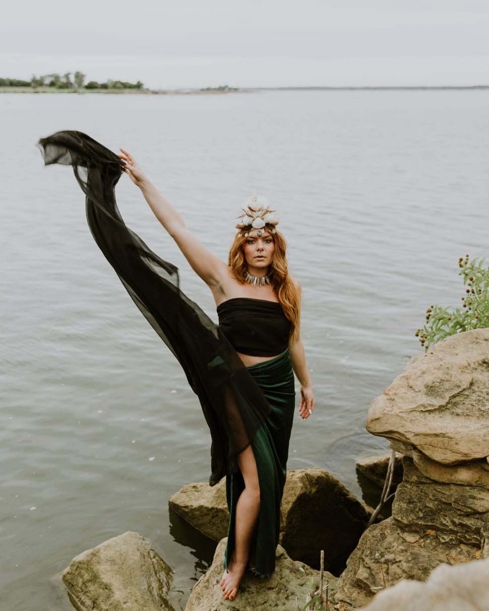 woman in black tube crop top and side slit maxi skirt on cliff beside water preview