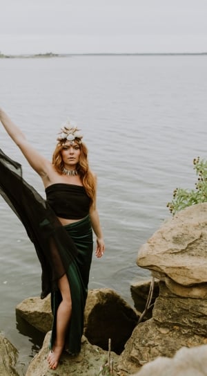 woman in black tube crop top and side slit maxi skirt on cliff beside water thumbnail